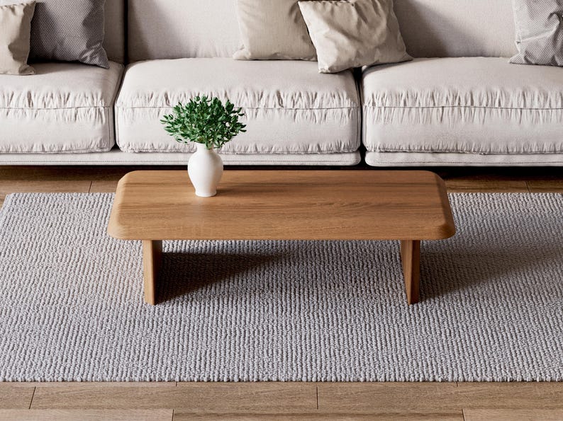 K&ouml;nnte beinhalten: Ein hellgrauer Teppich mit einem Holz-Couchtisch in der Mitte. Der Tisch hat eine nat&uuml;rliche Holzoptik und eine einfache rechteckige Form. Eine kleine Topfpflanze steht auf dem Tisch.