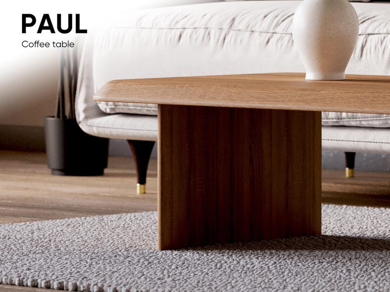 K&ouml;nnte beinhalten: Ein Holz-Couchtisch mit einer rechteckigen Tischplatte und einem einzigen, dicken, rechteckigen Bein. Der Tisch steht auf einem hellgrauen Teppich. Der Tisch ist mit "PAUL Coffee table" beschriftet.