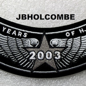 Puede incluir: Parche bordado negro con el texto "20 YEARS OF H.O.G. 2003" y el nombre "JBHOLCOMBE". El parche presenta un diseño de estrella y alas en plata y blanco.