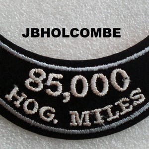 May include: Black motorcycle patch with white embroidered text that reads "85,000 HOG MILES".
