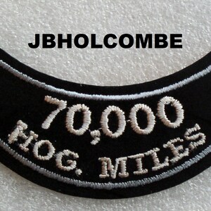 May include: Black motorcycle patch with white embroidered text "70,000 HOG MILES" and the name "JBHOLCOMBE" above.