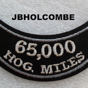 May include: Black motorcycle patch with white embroidered text that reads "65,000 HOG MILES".