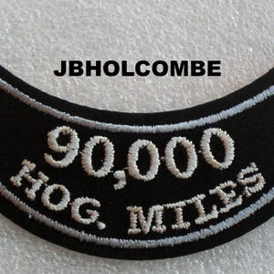 May include: Black motorcycle patch with white embroidered text that reads "90,000 HOG MILES".