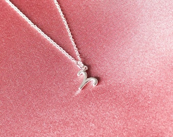 May include: A silver necklace with a small, stylized ram pendant on a pink satin background.