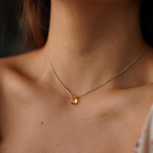 May include: A gold chain necklace with a teardrop-shaped amber gemstone pendant.