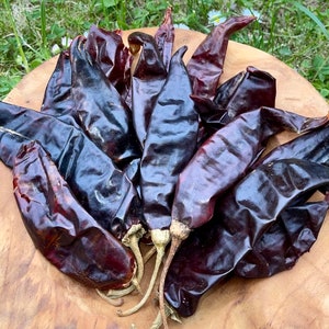 Op de afbeelding: Een verzameling gedroogde donkerrode chilipepers op een houten oppervlak. De pepers zijn lang en dun, met een licht gerimpelde textuur.