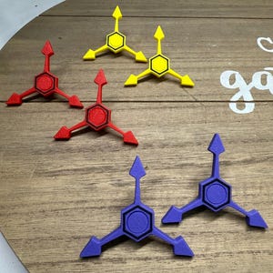 May include: A collection of colorful, geometric shapes in red, yellow, and purple. Each shape features a central hexagon with three radiating arrow-like points. The objects are arranged on a wooden surface.
