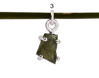 May include: A silver charm with a dark green, rough, irregular shaped stone. The stone is set in silver and has a silver loop at the top for attaching to a bracelet or necklace.