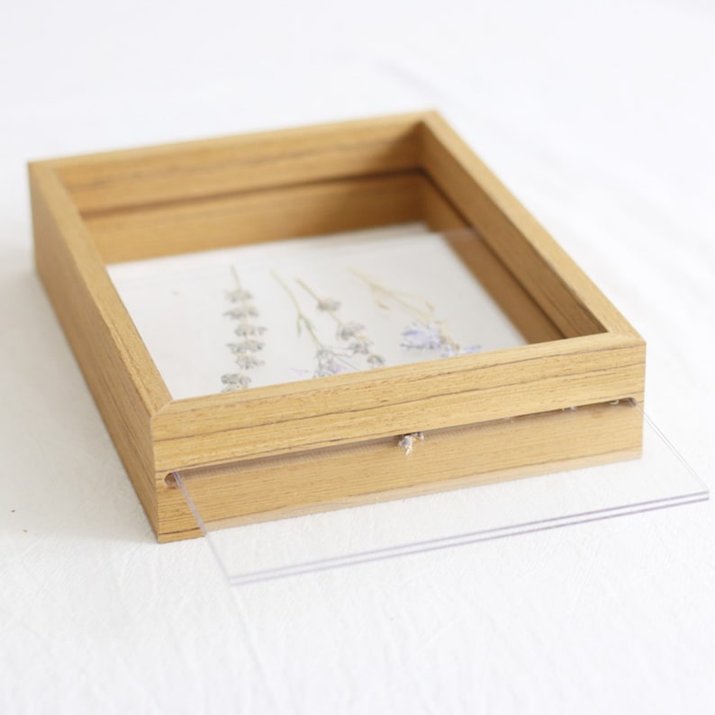 May include: A wooden picture frame with a clear acrylic front, showcasing dried flowers. The frame has a natural wood finish and a simple, rectangular design.