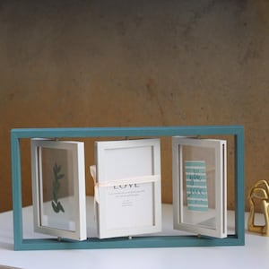 May include: A teal rectangular frame containing three rotating white picture frames. The centre frame features a light pink ribbon and the text "LOVE" printed on the insert, while the right frame displays a card with the text "you rock".