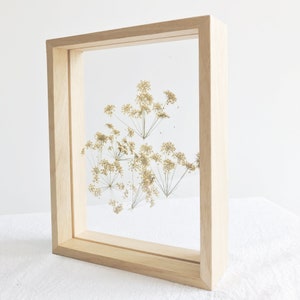 May include: A framed pressed flower art piece with dried, light brown flowers in a natural wood frame.