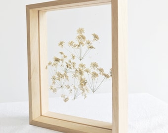 May include: A framed pressed flower art piece with dried, light brown flowers in a natural wood frame.