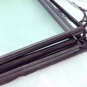 May include: A set of four black metal picture frames with glass panels. The frames are stacked on top of each other and are connected by a chain.