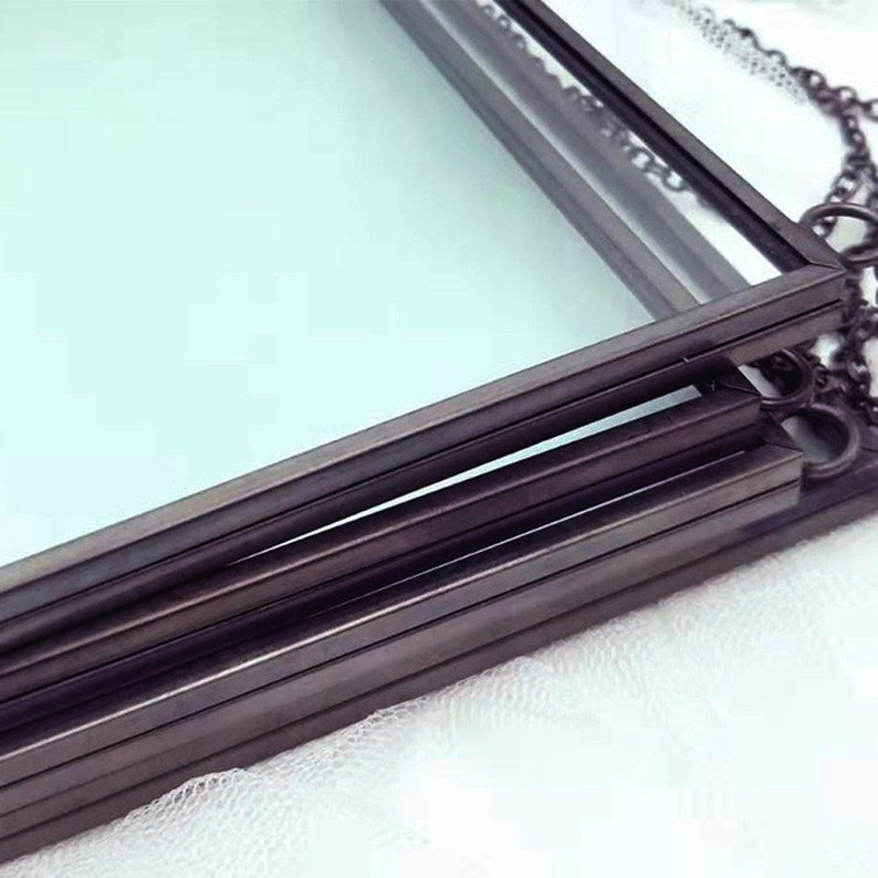 May include: A set of four black metal picture frames with glass panels. The frames are stacked on top of each other and are connected by a chain.