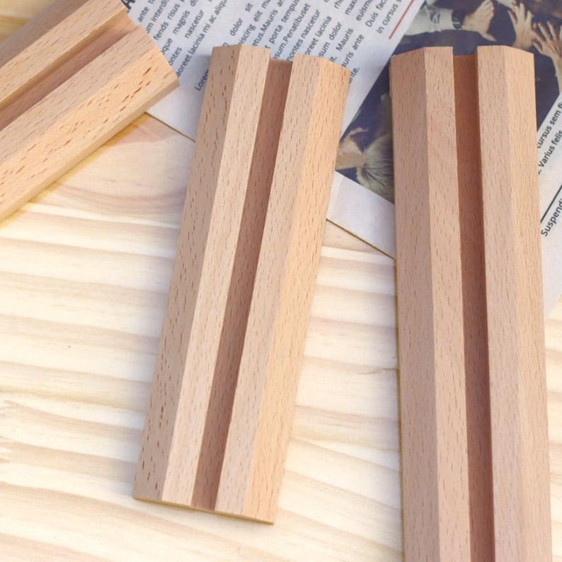 May include: Three wooden display stands with a slot in the center. The stands are made of light brown wood and have a natural finish.