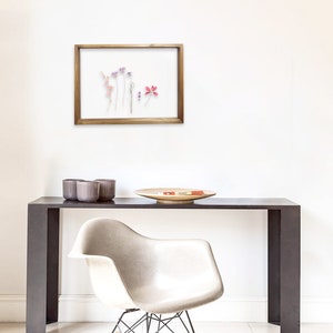 May include: A framed pressed flower display featuring a selection of dried flowers in shades of pink, purple, and white. The frame is made from natural wood and has a clear glass front.