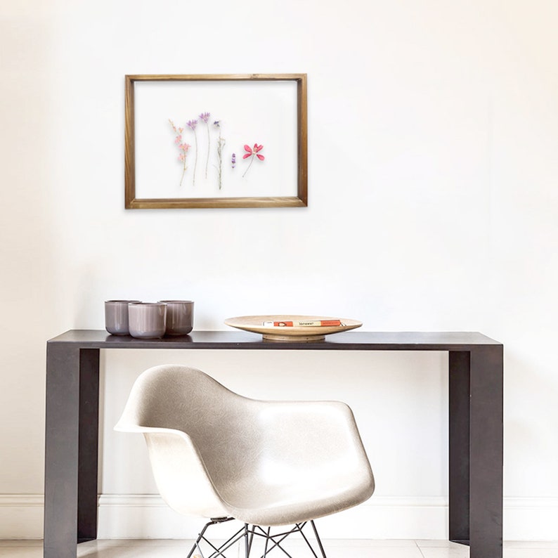 May include: A framed pressed flower display featuring a selection of dried flowers in shades of pink, purple, and white. The frame is made from natural wood and has a clear glass front.
