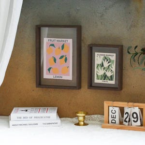 May include: Two framed prints with a minimalist design. The left print features a pink background with yellow lemons and the text "Fruit Market, Lemon". The right print features a green background with white flowers and the text "Flower Market, Tokyo".