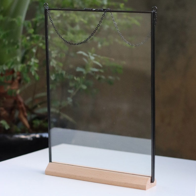 May include: A black metal frame with a clear glass panel and a wooden base. The frame has two chains attached to the top for hanging.