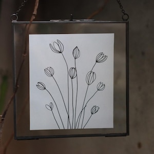 May include: A black and white line drawing of a bouquet of flowers in a simple glass frame.