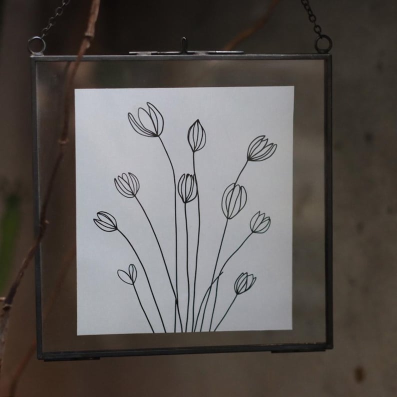 May include: A black and white line drawing of a bouquet of flowers in a simple glass frame.