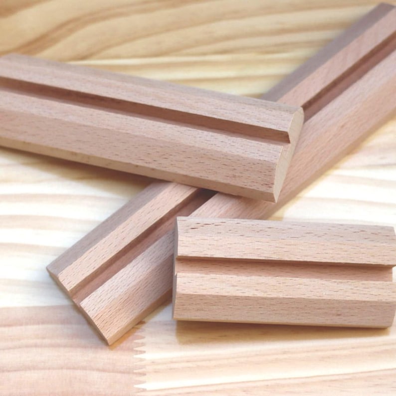 May include: Three wooden pieces with a groove cut into the top. The pieces are light brown and have a smooth finish.