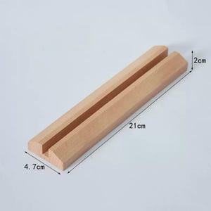 May include: A wooden phone stand with a slot for holding a phone. The stand is 21 cm long, 2 cm wide, and 4.7 cm tall.