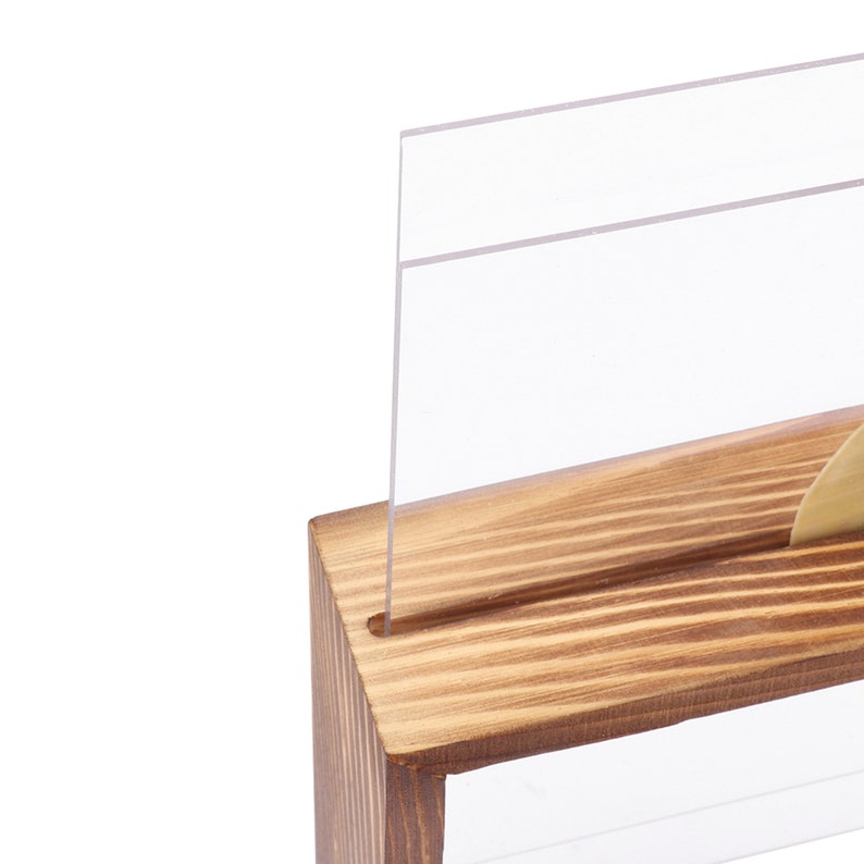 May include: A wooden sign holder with a clear acrylic sign insert. The holder has a natural wood finish and a slot for the sign to be inserted.