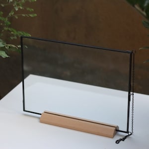May include: A black metal frame with a clear glass panel and a wooden stand. The frame has a chain attached to the side.