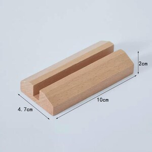 May include: A wooden phone stand with a slot for holding a phone. The stand is 10 cm long, 4.7 cm wide, and 2 cm high.