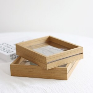 May include: Two wooden picture frames with a clear glass insert. The frames are stacked on top of each other. The top frame is slightly larger than the bottom frame.