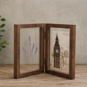 Puede incluir: Un marco de fotos doble articulado hecho de madera marrón oscura con textura rústica. El lado izquierdo contiene ramas de lavanda morada prensadas entre dos cristales. El lado derecho muestra una impresión vintage de la torre Big Ben.