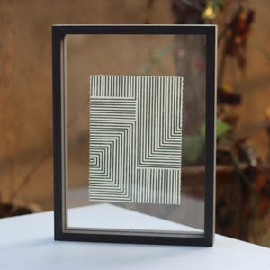 May include: A black framed picture with a white background and a black and white geometric design.