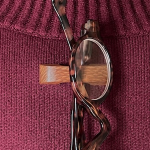 May include: A pair of tortoiseshell reading glasses with a wooden clip on a burgundy sweater.