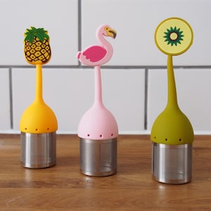 May include: Three colourful tea infusers with different designs: a pineapple, a flamingo, and a green circle with a yellow centre. Each infuser has a stainless steel mesh filter.