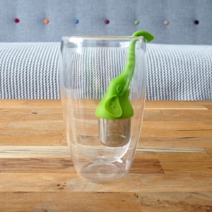 May include: Green silicone tea infuser shaped like an elephant with a stainless steel mesh filter inside a clear glass mug.