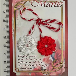 May include: A red and white martisor, a traditional Romanian charm, with a white flower and a red flower. The card reads "Martie" and "Un g&icirc;nd frumos şi un z&icirc;mbet din tot sufletul, un mărţişor, care să vă aducă &icirc;n suflet Primăvara!"