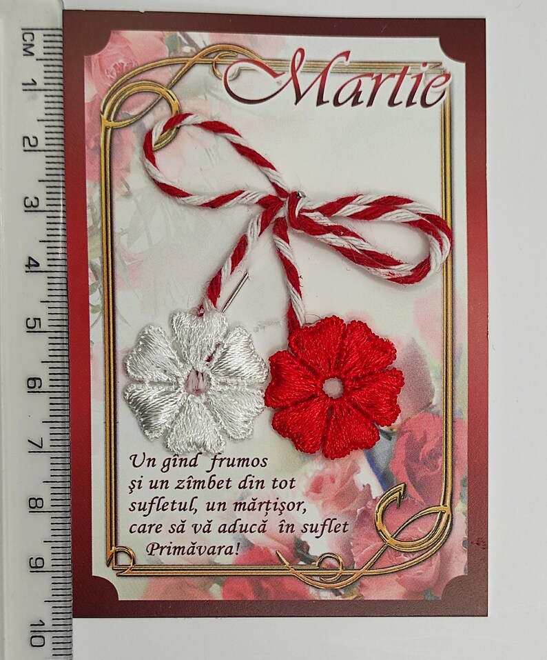 May include: A red and white martisor, a traditional Romanian charm, with a white flower and a red flower. The card reads "Martie" and "Un g&icirc;nd frumos şi un z&icirc;mbet din tot sufletul, un mărţişor, care să vă aducă &icirc;n suflet Primăvara!"