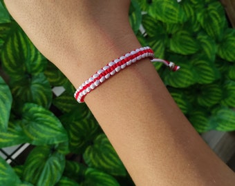 May include: A red and white braided friendship bracelet on a person's wrist.