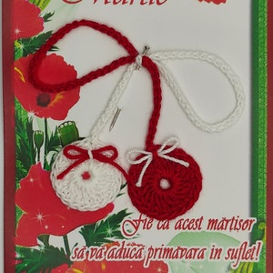 May include: A red and white crocheted martisor with a red bow and a white bow. The martisor is on a card with the name "Martie" and the text "Fie ca acest martisor sa va aduca primavara in suflet!"