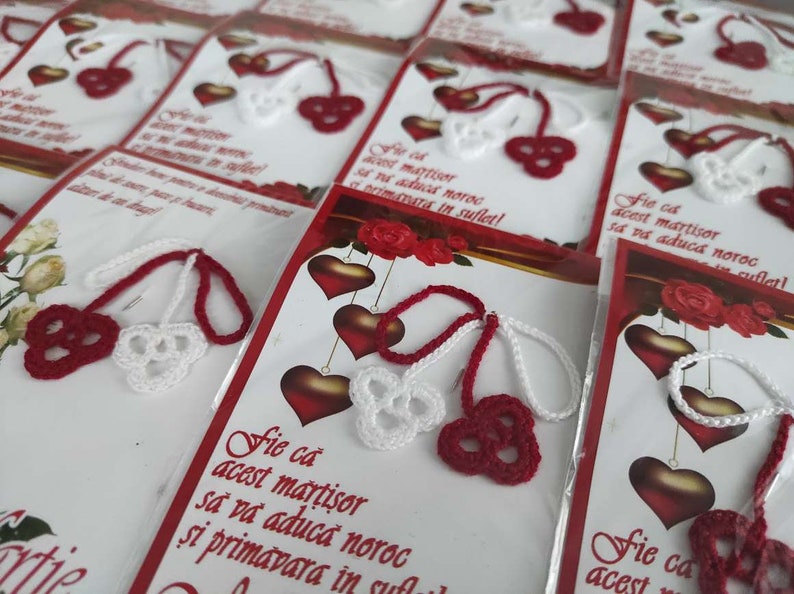 May include: A close-up of several red and white crocheted cherry charms with a message card that reads "Fie ca acest martisor sa va aducă noroc si primavara in suflet!"  The cards are packaged in clear plastic bags.