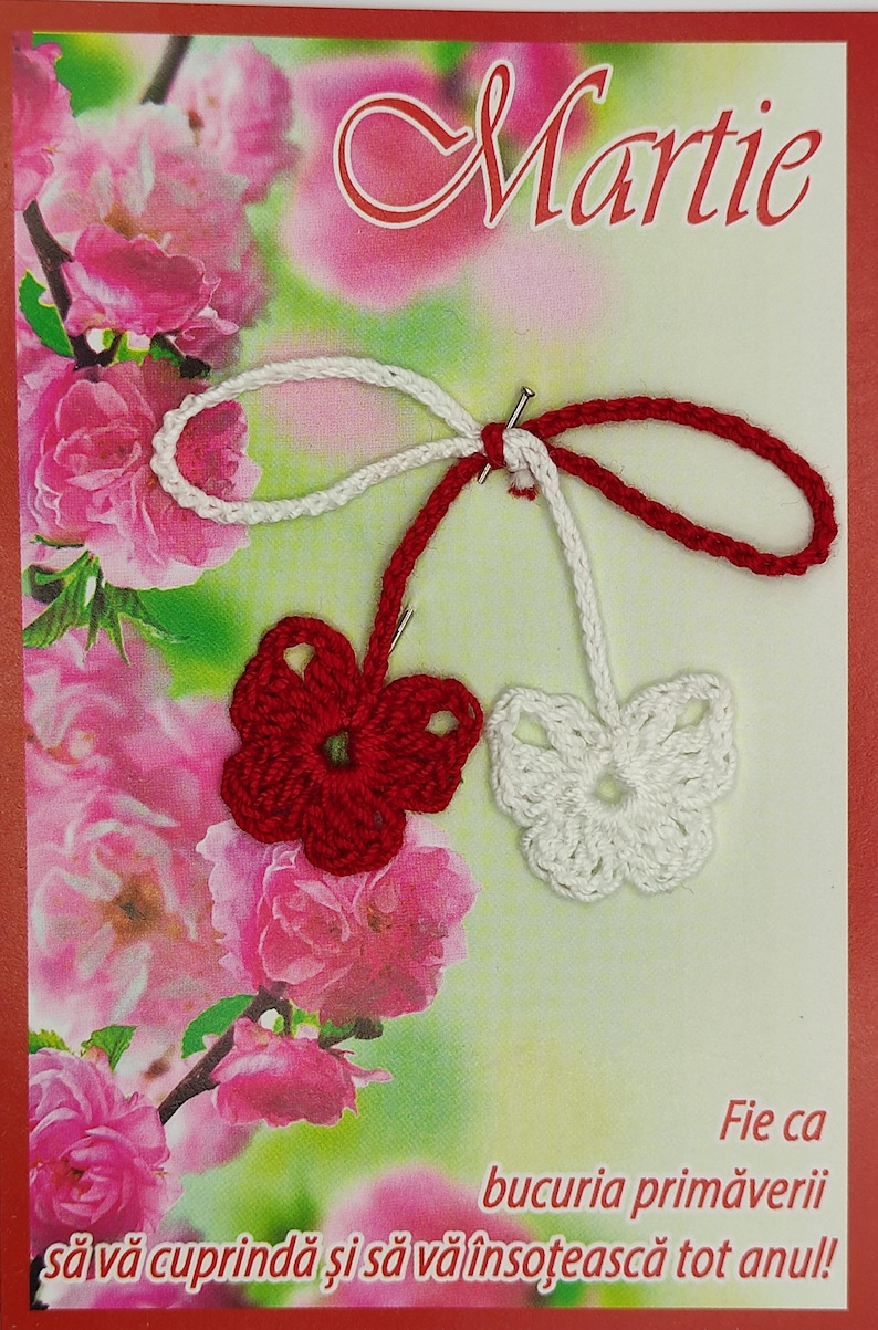 May include: A greeting card with a crocheted red and white flower charm. The card has a pink floral background and the text "Martie" and "Fie ca bucuria primaverii sa va cuprinda si sa va insoțească tot anul!"