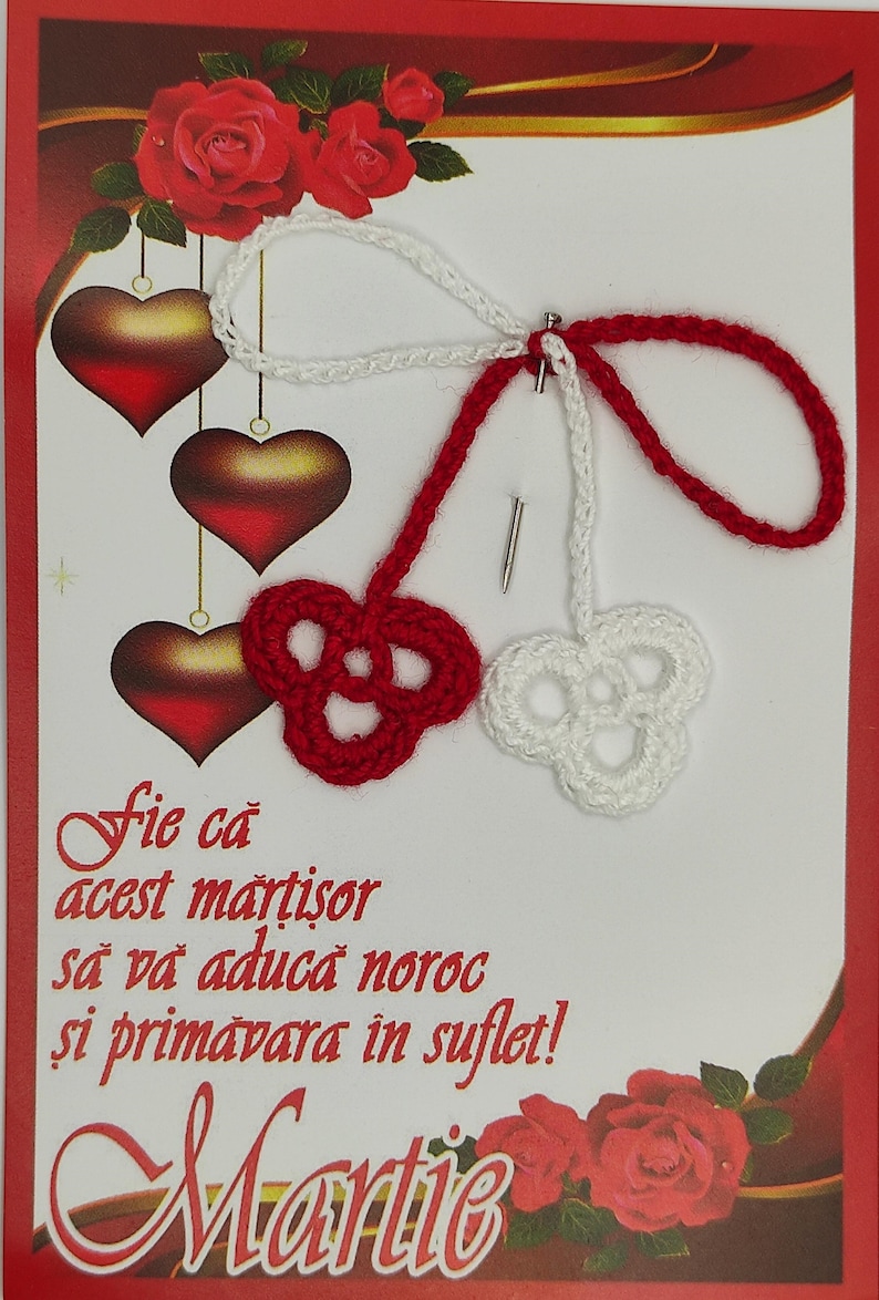 May include: A red and white crocheted martisor with a message that reads "Fie ca acest martisor sa va aduca noroc si primavara in suflet! Martie". The martisor is on a white card with red roses and hearts.