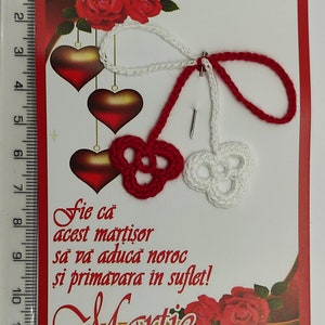 May include: A red and white crocheted martisor, a traditional Romanian charm, with the text "Fie ca acest martisor sa va aduca noroc si primavara in suflet!" and the word "Martie" on a red card with a gold border and red roses.