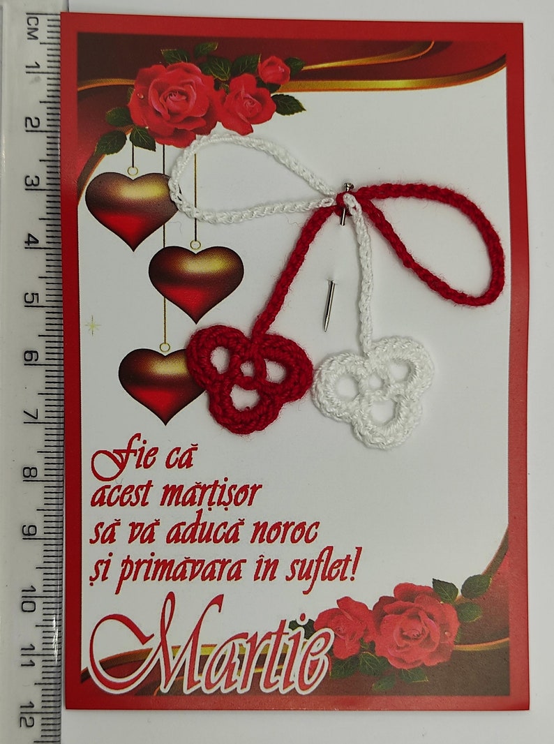 May include: A red and white crocheted martisor, a traditional Romanian charm, with the text "Fie ca acest martisor sa va aduca noroc si primavara in suflet!" and the word "Martie" on a red card with a gold border and red roses.