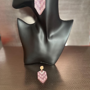 May include: Hexagon-shaped beaded earrings in shades of pink and white, displayed on a black mannequin head. The earrings have a gold-coloured stud and a geometric pattern. The second earring is shown separately.