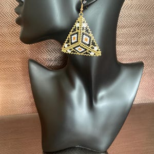 May include: A pair of triangular earrings with a geometric pattern in black, white, and gold beads.