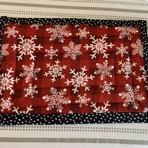 May include: Red and black quilted placemat with a snowflake pattern. The placemat has a black and white polka dot border.