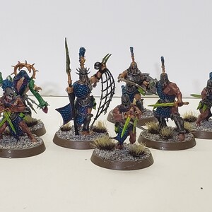 Könnte beinhalten: Eine Gruppe von neun bemalten Miniaturfiguren, die jeweils auf einer runden Basis stehen. Die Figuren sind in blauer und grüner Rüstung gekleidet, mit verschiedenen Waffen und Accessoires. Die Figuren stehen vor einem weißen Hintergrund.
