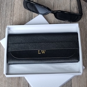 以下が含まれることがあります： 金色の「LW」のイニシャルが刻まれた黒い革製の眼鏡ケース。ケースは白い箱に入っています。